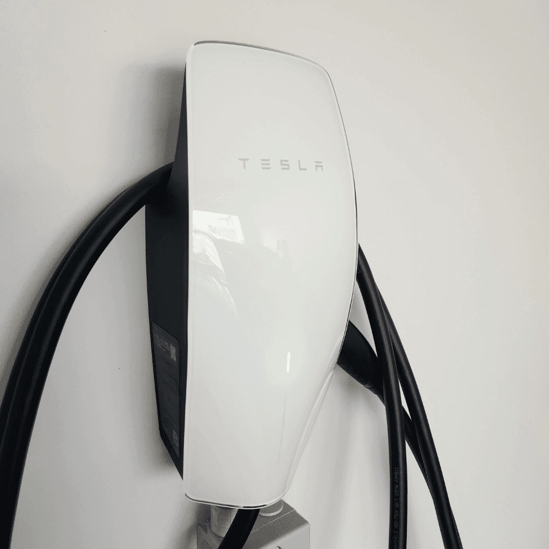Tesla Gen 3 Wall Connector EV charger mounted on a white interior wall with a sleek, glossy white front panel displaying the Tesla logo, thick black charging cable, and green indicator light Tesla Gen 3 Wall Connector EV charger mounted on a white interior wall with a sleek, glossy white front panel displaying the Tesla logo, thick black charging cable, and green indicator light